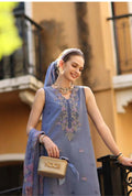 Woman in a blue embroidered dress holding a beige handbag, standing in front of a building.