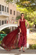 Woman in a red dress with a long scarf standing outdoors near a bridge.