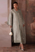 Woman in a traditional outfit with intricate designs standing against a decorative wall.