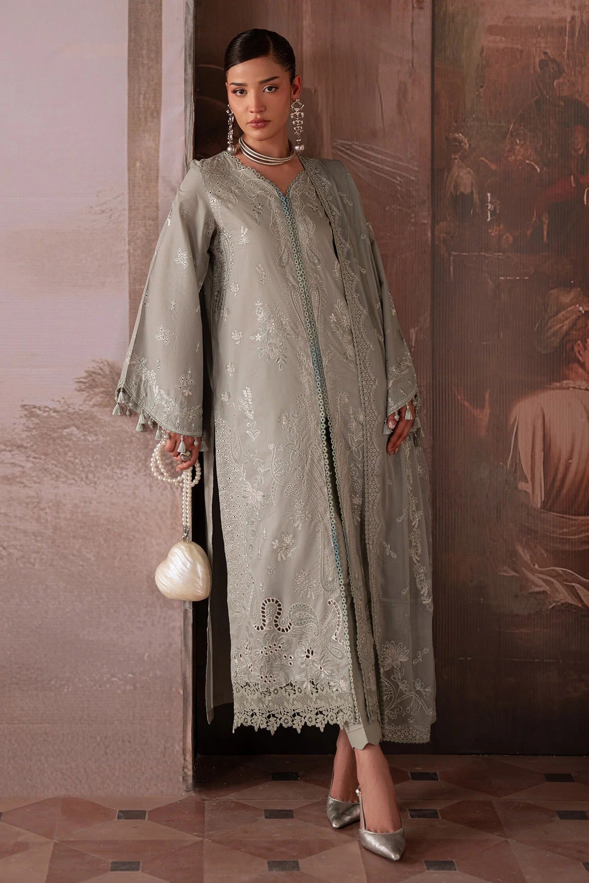Woman in a traditional outfit with intricate designs standing against a decorative wall.