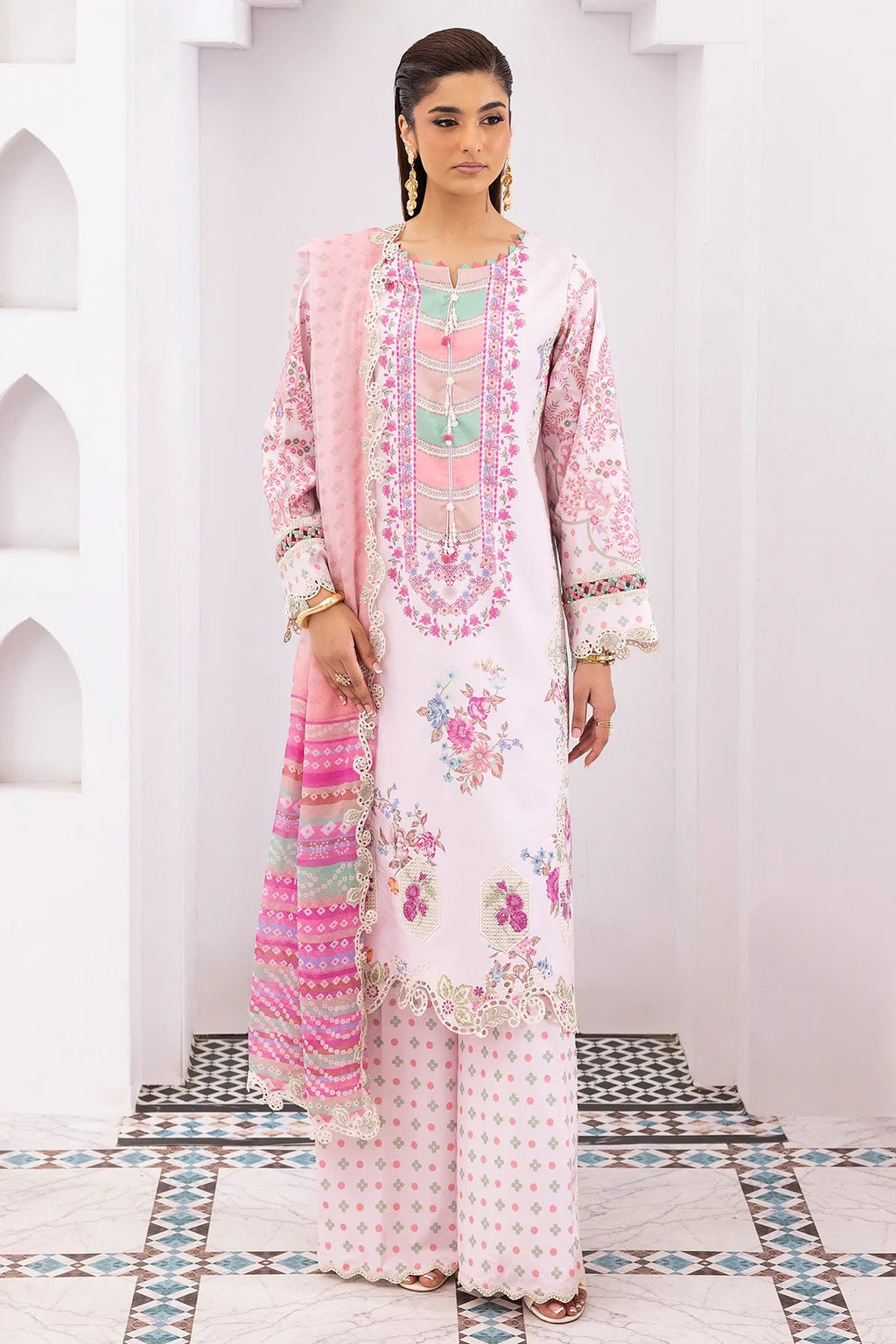 Woman wearing a pink and white embroidered traditional outfit with a matching dupatta in a decorative setting.