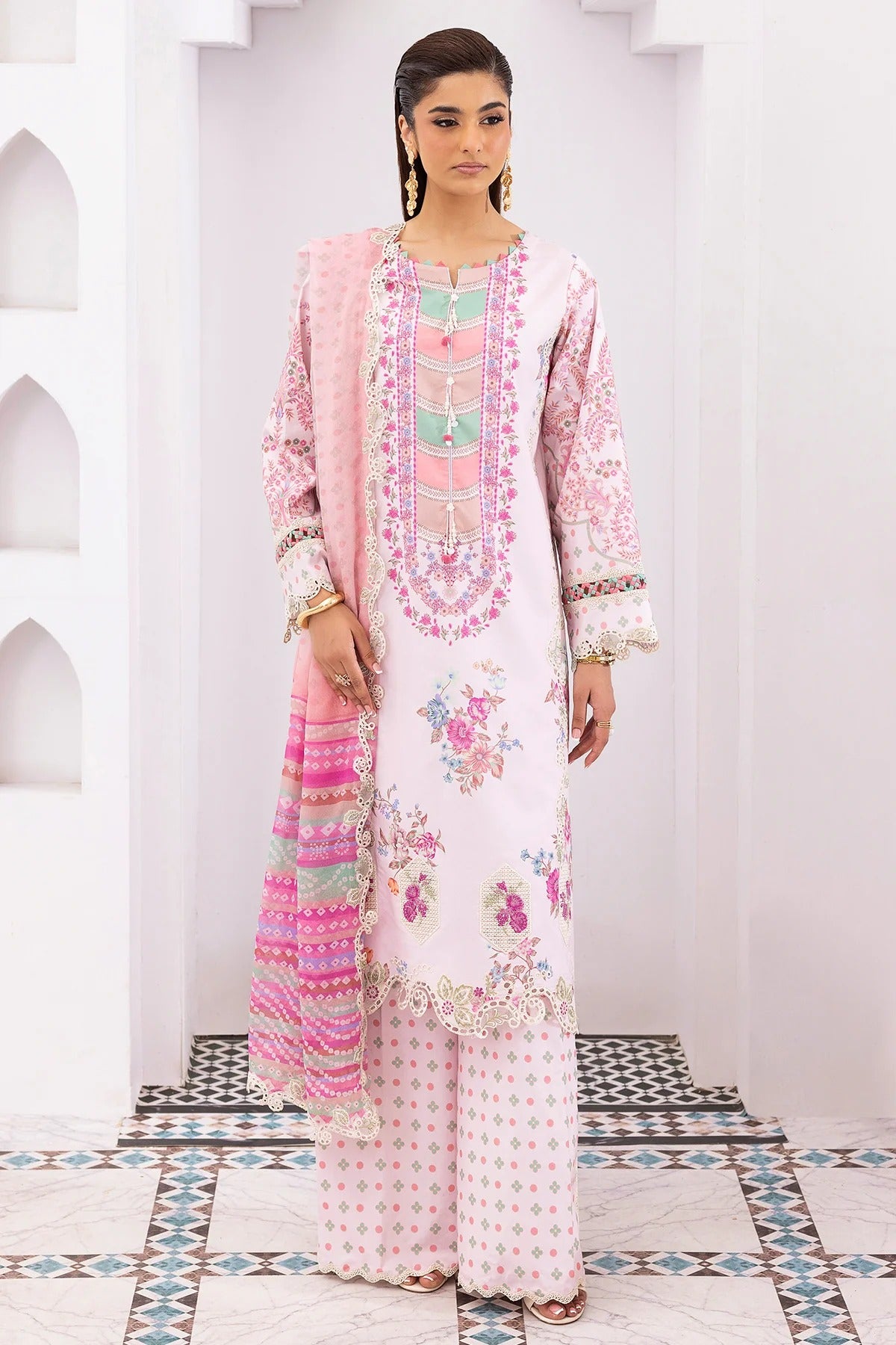 Woman wearing a pink and white embroidered traditional outfit with a matching dupatta in a decorative setting.