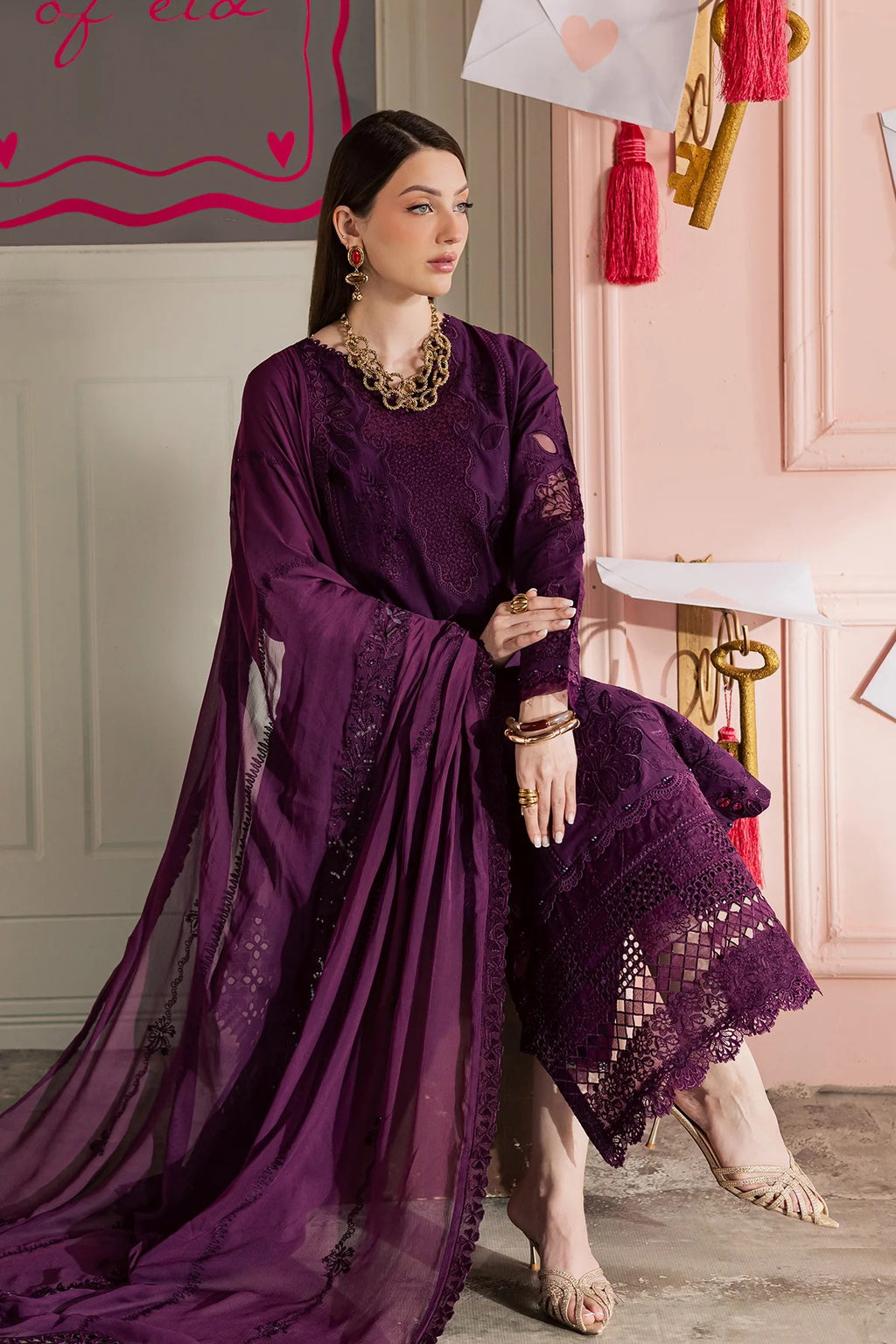 Woman in a purple traditional outfit with intricate designs, sitting indoors.