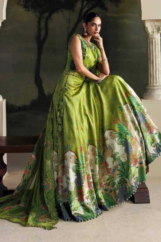 A woman models a voluminous green saree with a tropical floral and scenic print, seated in an elegant indoor setting with a painted backdrop.