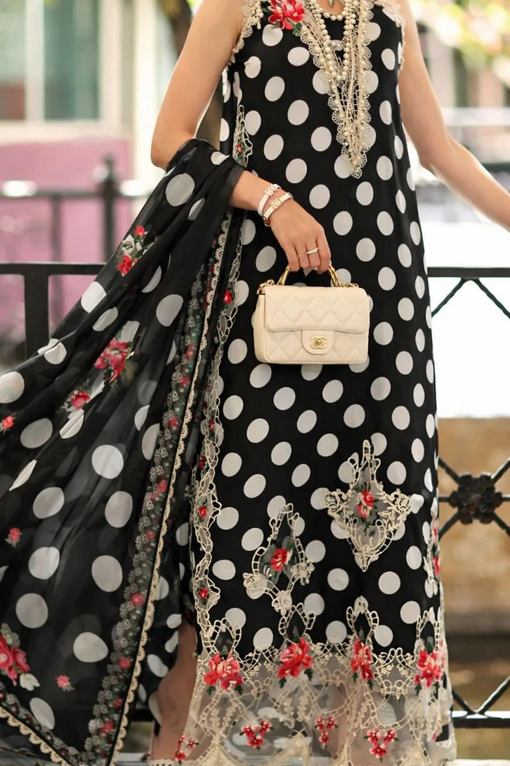 Person wearing a black polka dot dress with floral and lace details, holding a cream handbag.