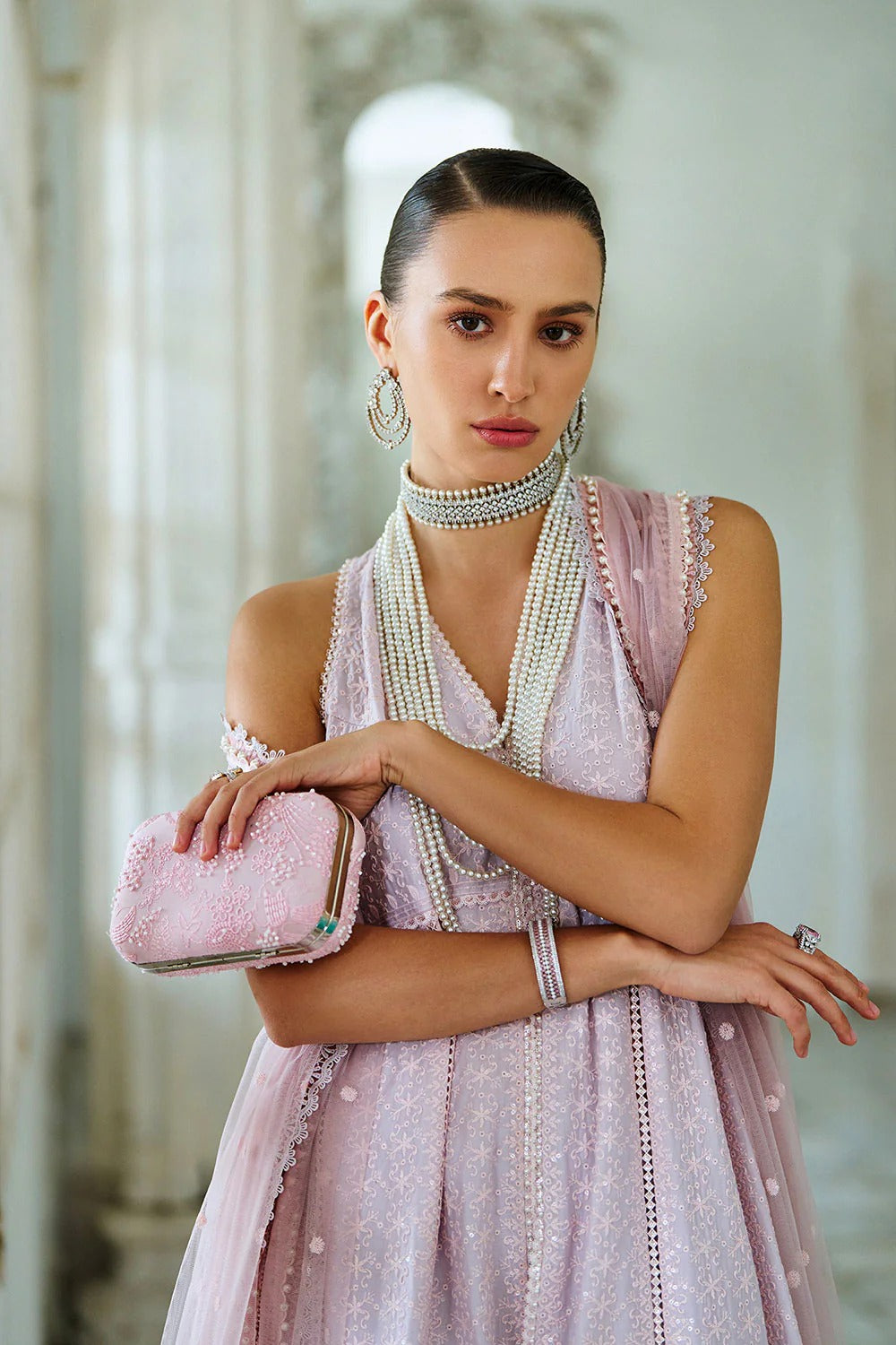Woman in a light pink dress with pearl accessories holding a pink clutch.