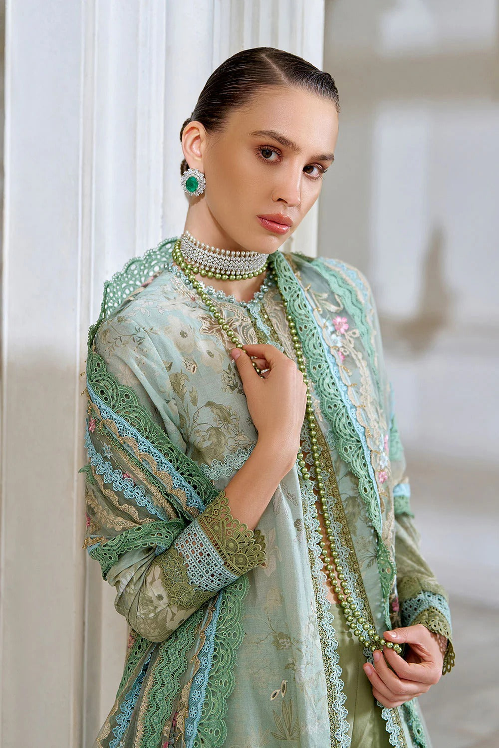 Woman wearing a light green traditional outfit with intricate patterns and jewelry indoors.