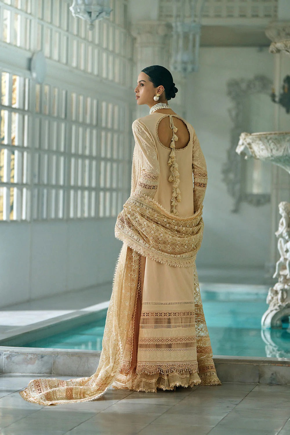 Woman in a traditional embroidered outfit standing by a pool with decorative elements.