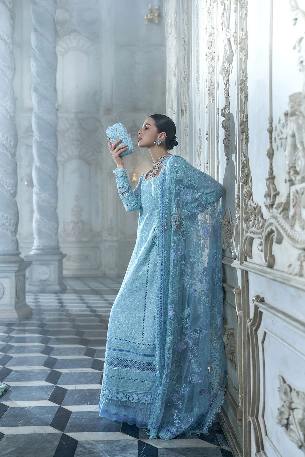 Woman in a light blue traditional outfit standing in an ornate hallway.