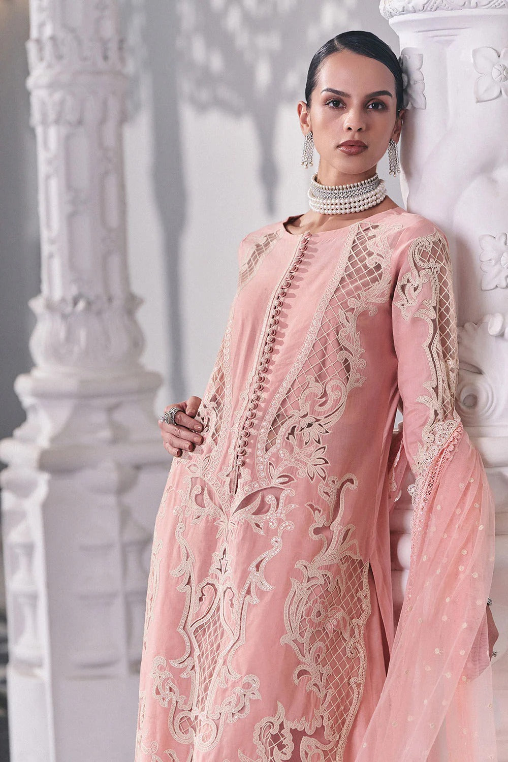 Woman wearing a pink embroidered outfit against a white architectural background