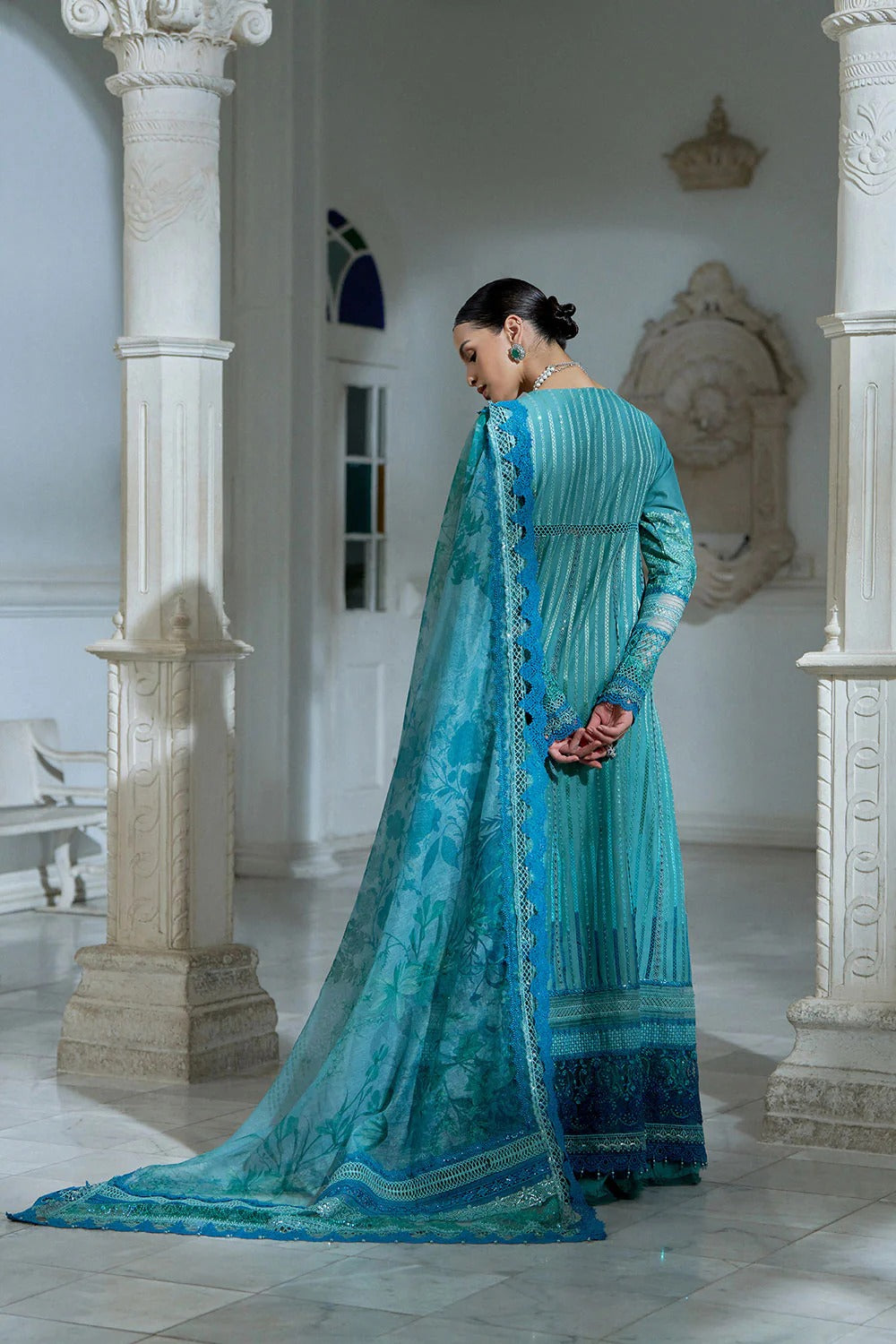Woman in a turquoise traditional outfit standing in an elegant indoor setting.