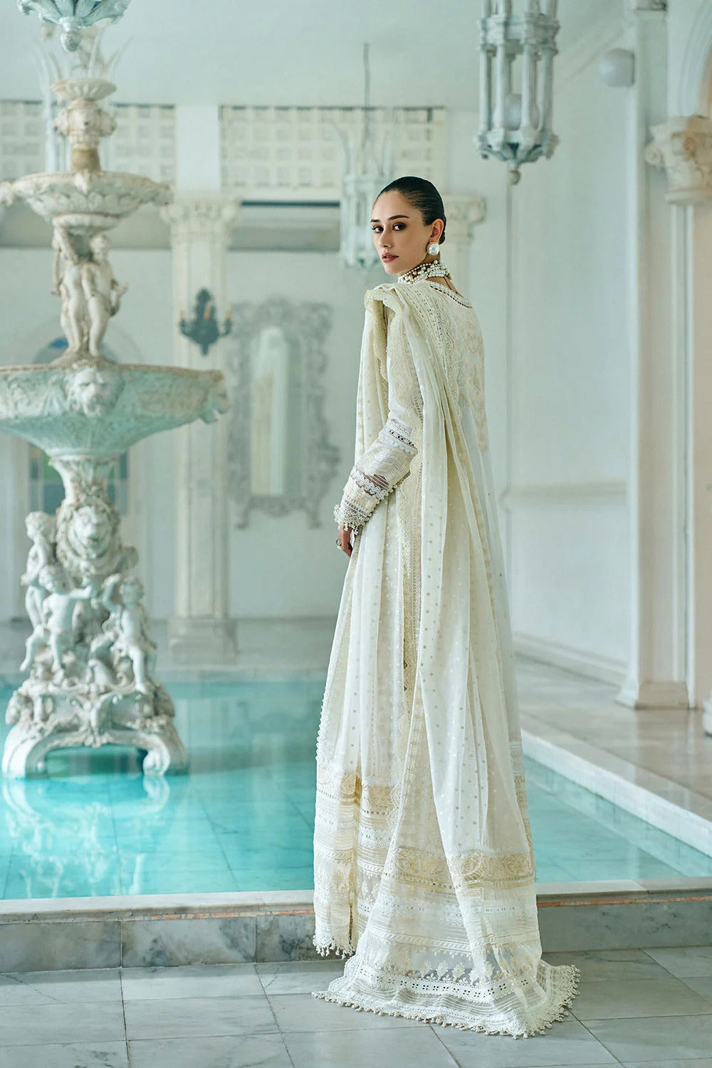 Woman in a white traditional outfit standing by a pool with decorative fountain