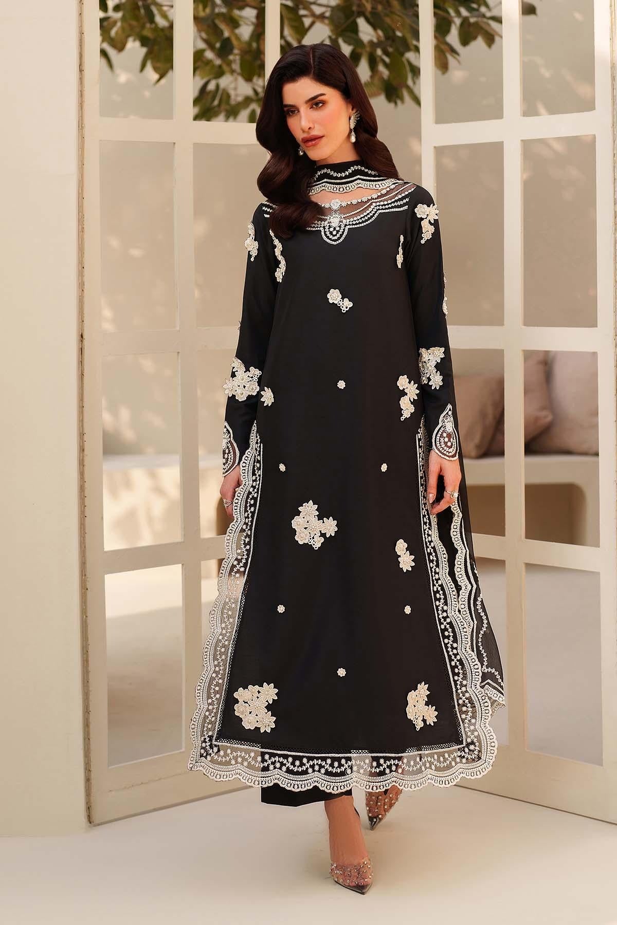 Woman wearing a black dress with white floral embroidery in a room with large windows.