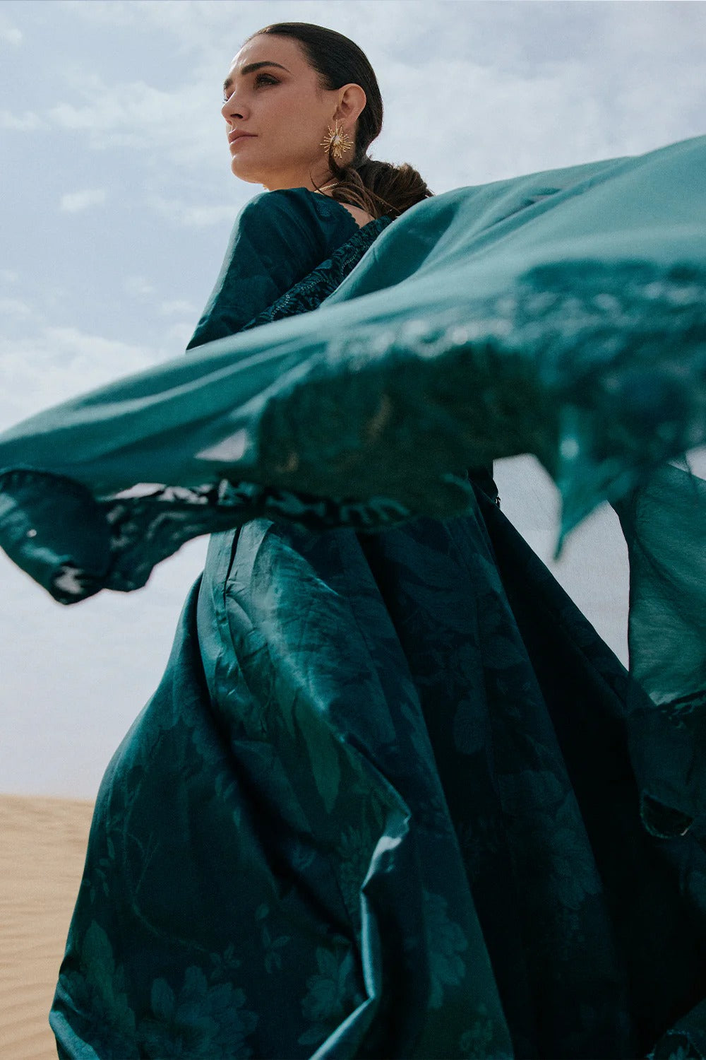 Woman in a teal dress with a flowing fabric against a desert backdrop