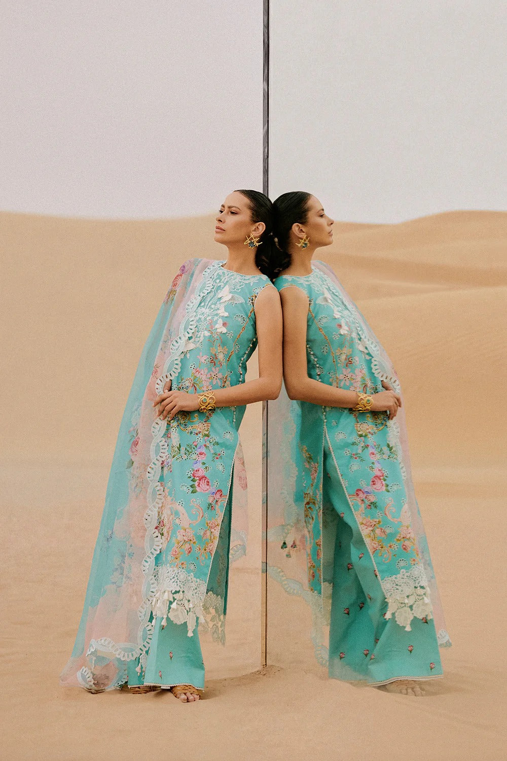 Woman in a turquoise embroidered outfit standing in sand dunes