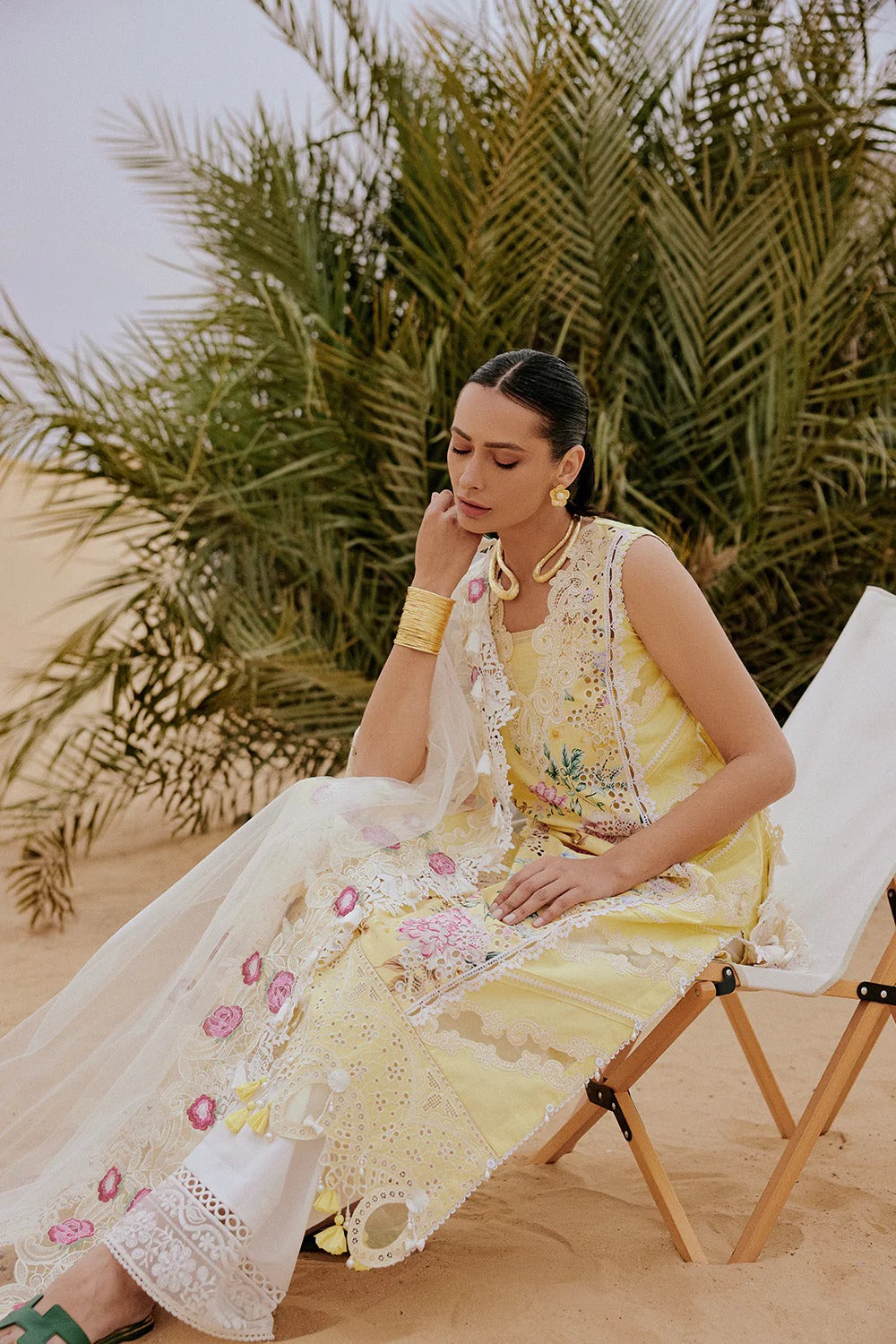 Woman in a yellow embroidered dress sitting on a chair with greenery in the background