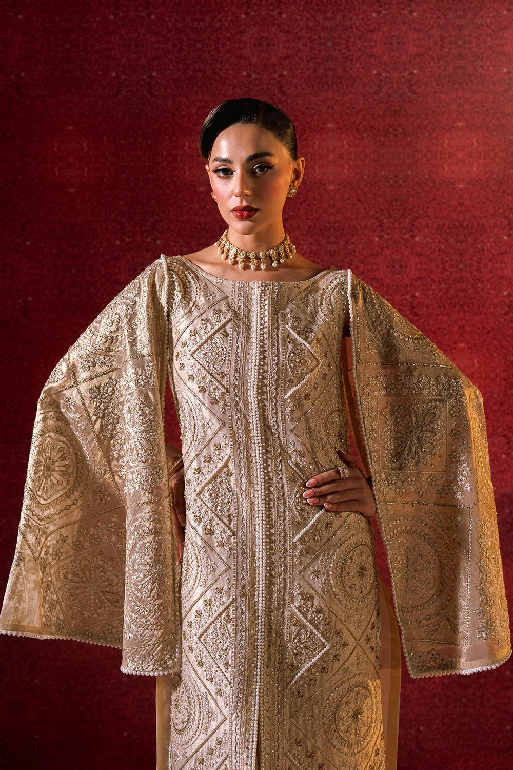 Woman wearing an intricately designed beige garment against a red background