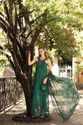 Woman in a green dress standing next to a tree in a park-like setting