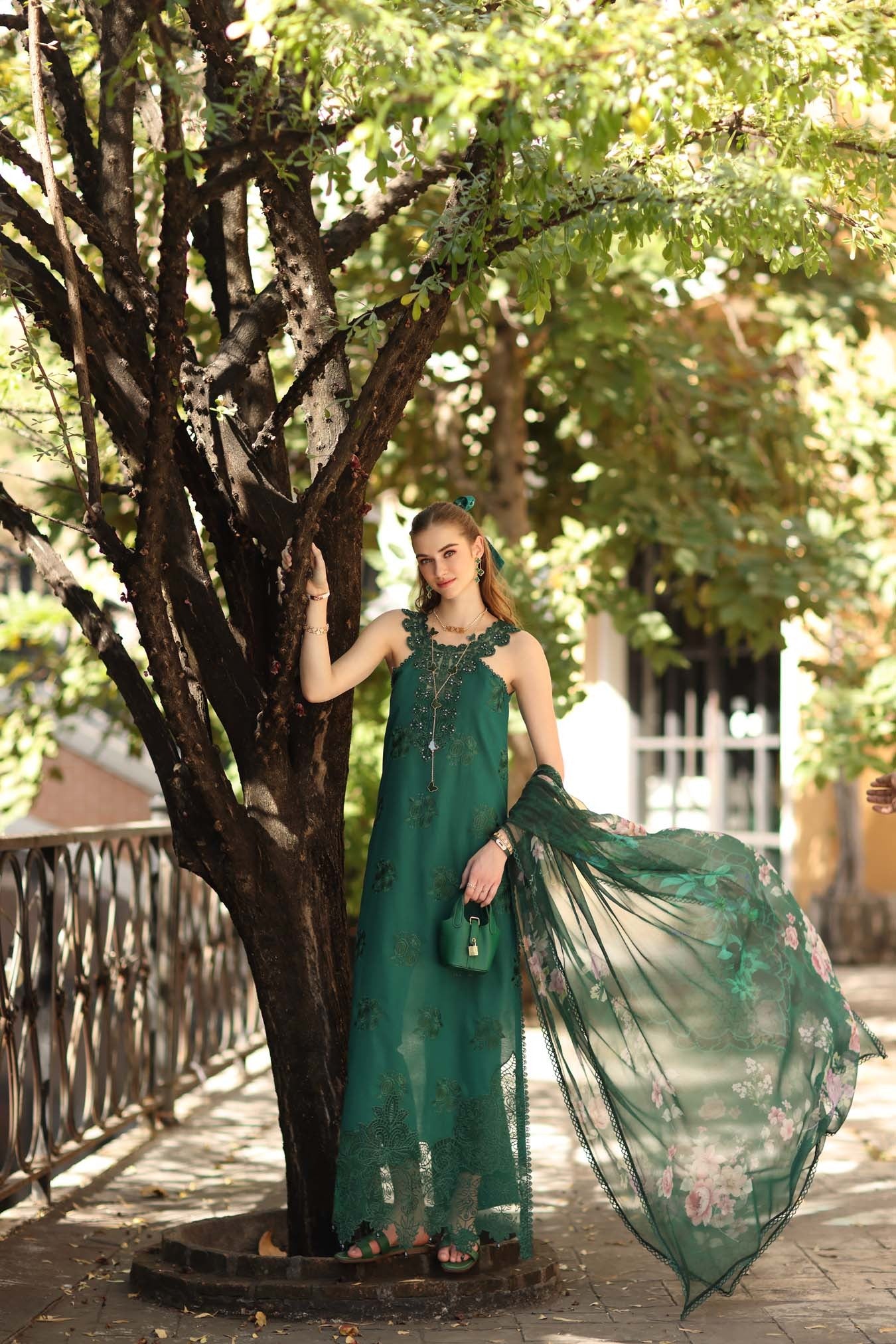Woman in a green dress standing next to a tree in a park-like setting