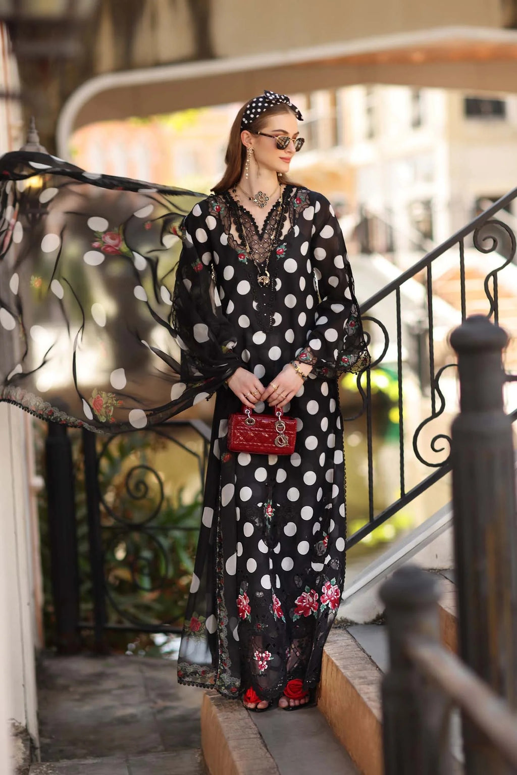 Woman in a black polka dot dress with floral embroidery standing on a staircase.