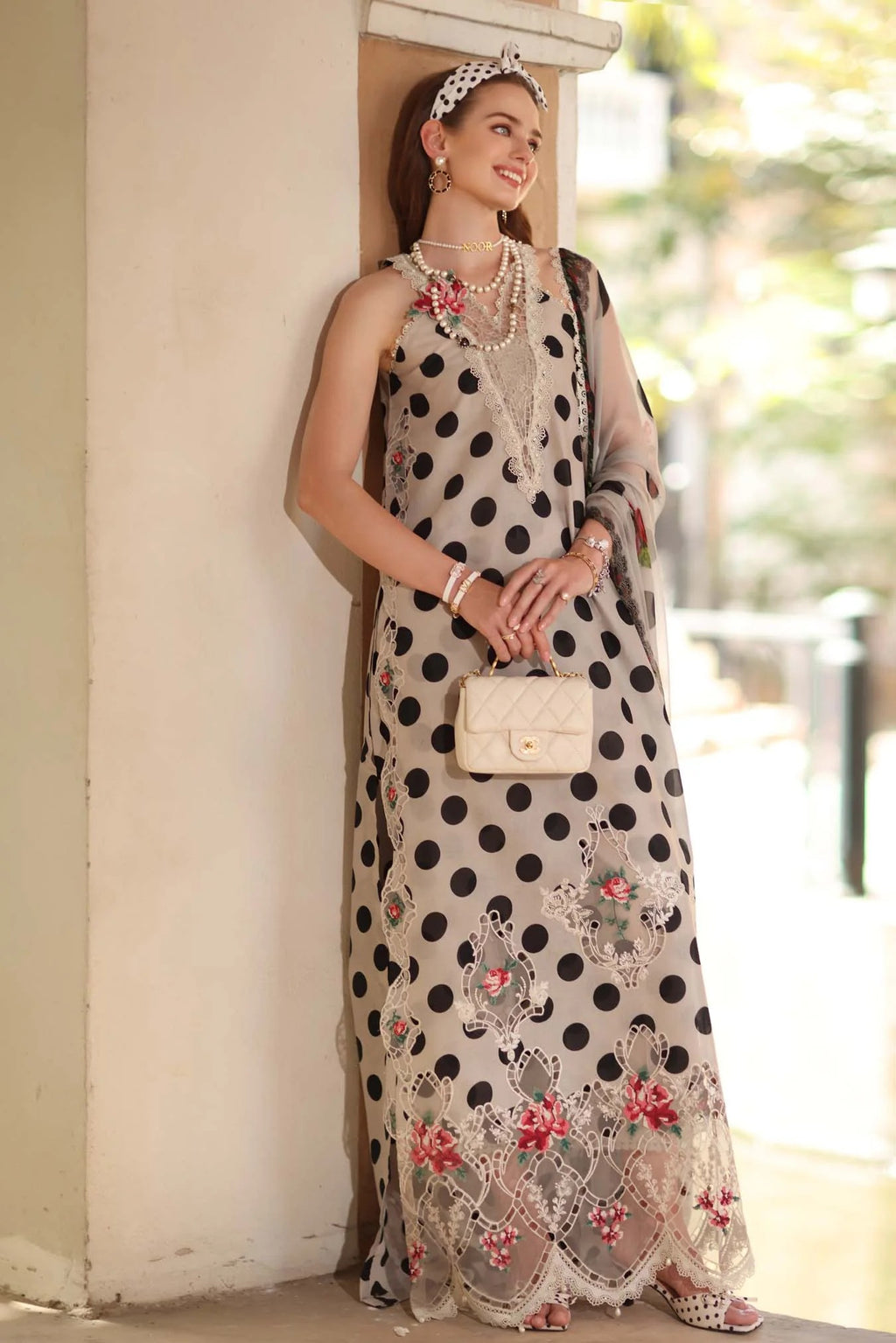 Woman in a polka dot dress with floral details standing against a wall.