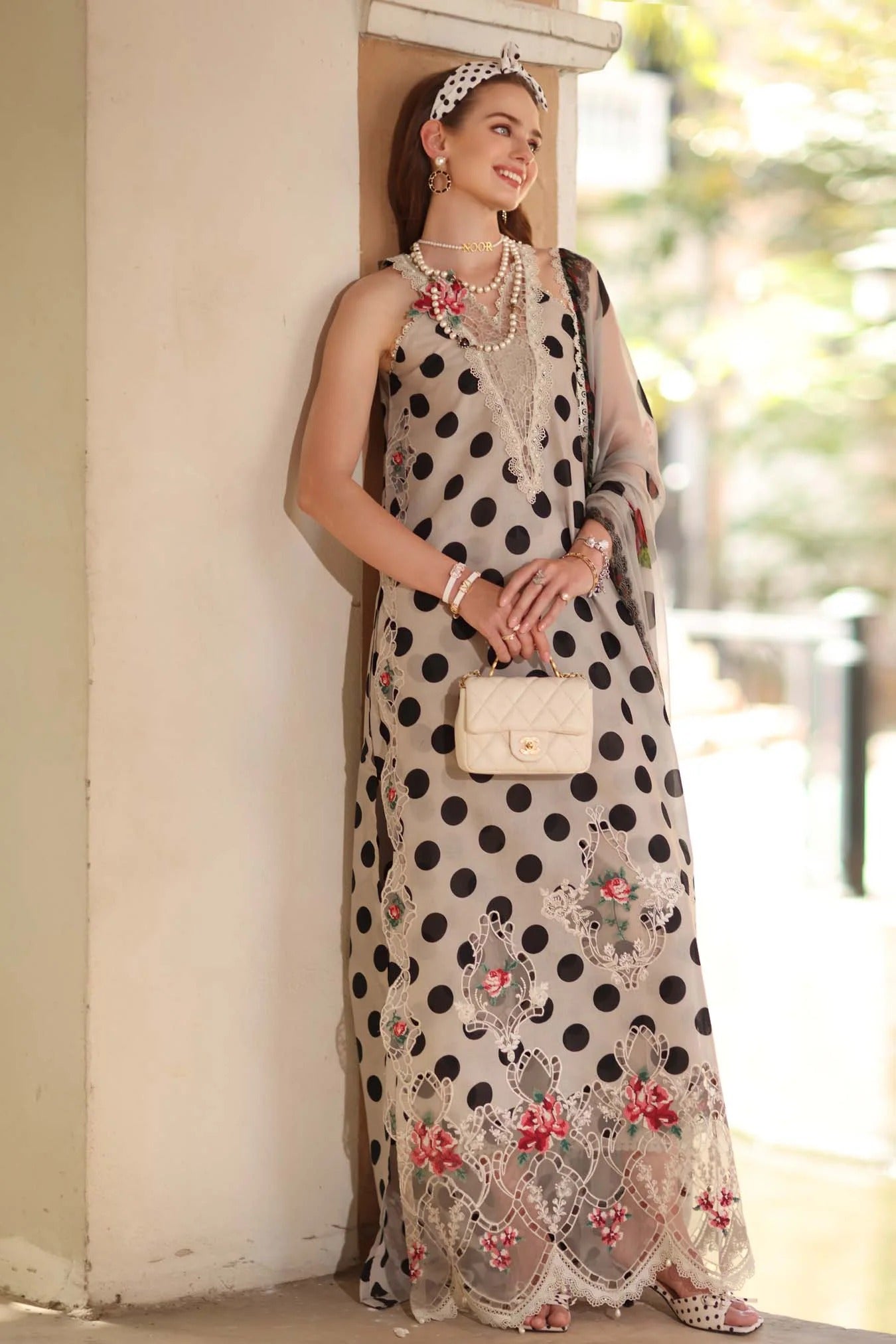 Woman in a polka dot dress with floral details standing against a wall.