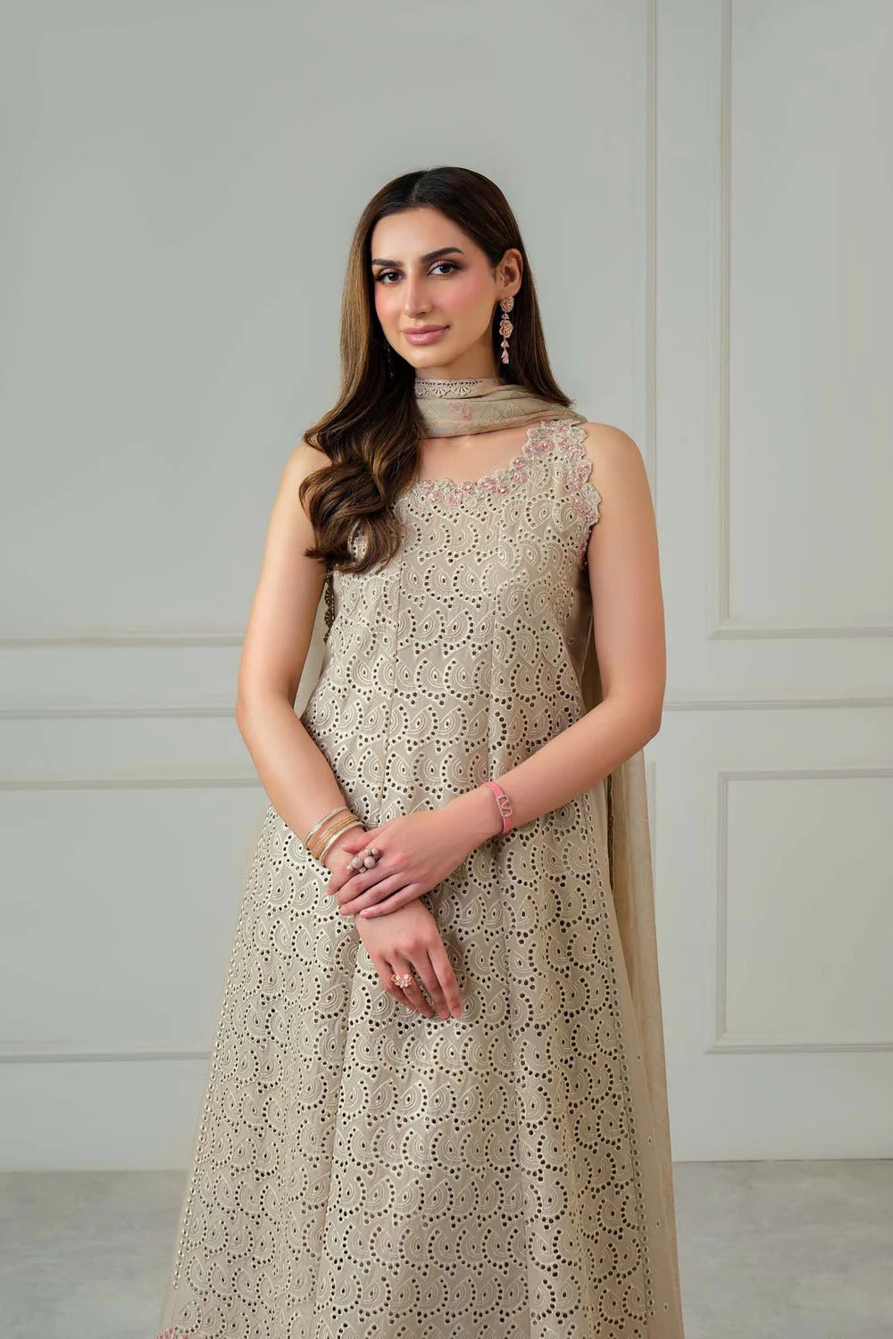Woman wearing a beige lace dress against a white wall