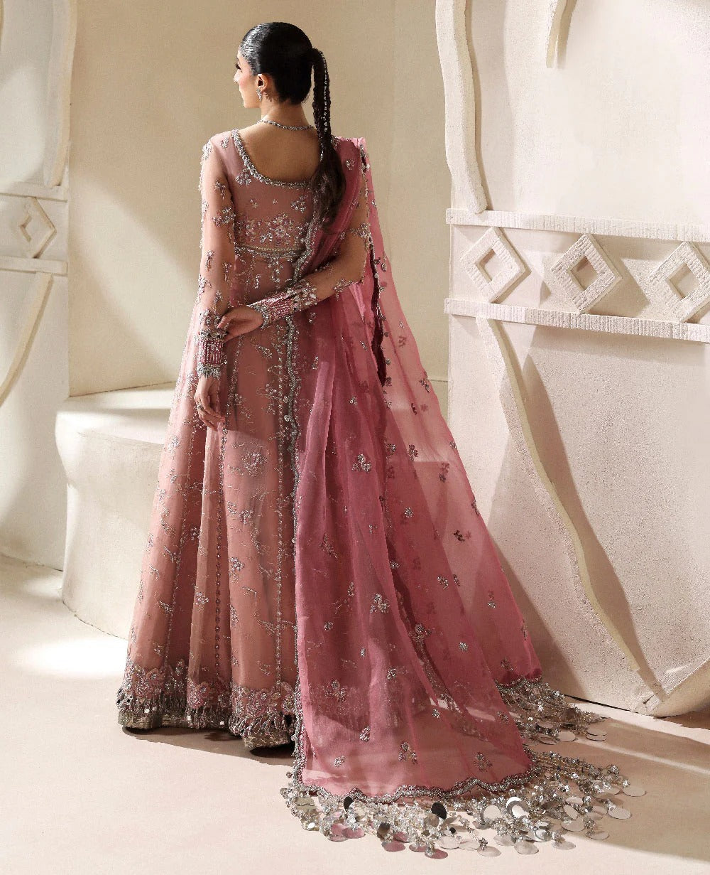 Woman in a pink embroidered traditional outfit standing in a decorative interior setting.