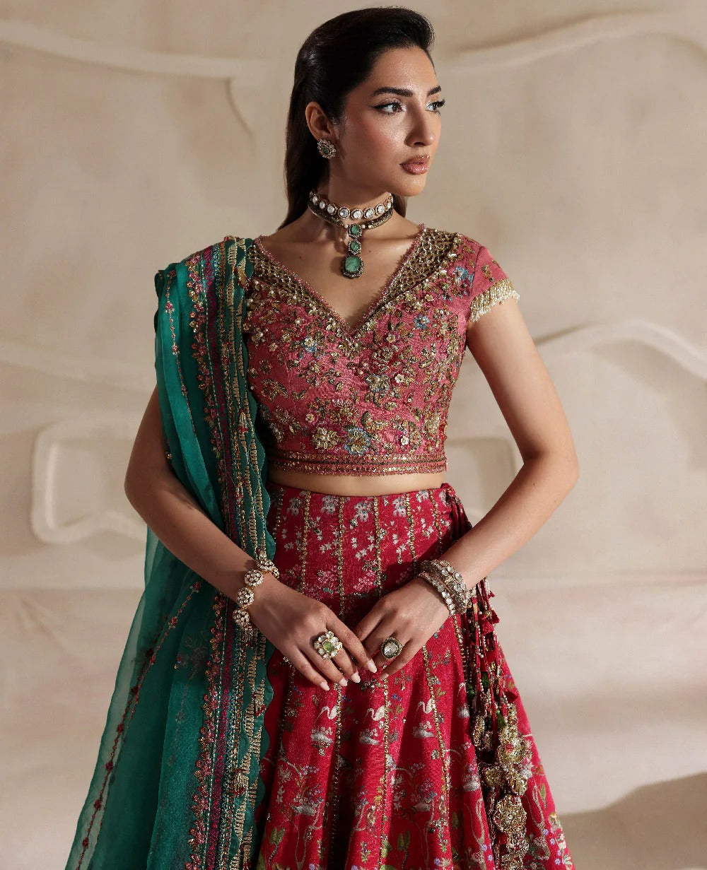 Woman in a red and green traditional outfit with jewelry against a neutral background