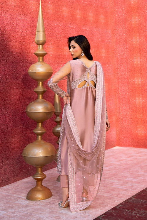 Woman in a pink traditional outfit standing against a pink wall with decorative elements.