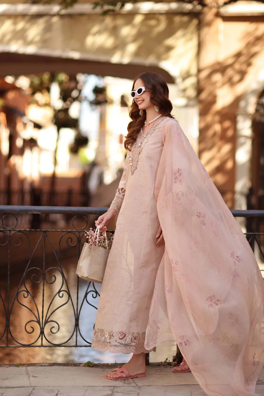 Woman in a light pink traditional outfit standing outdoors with a blurred background