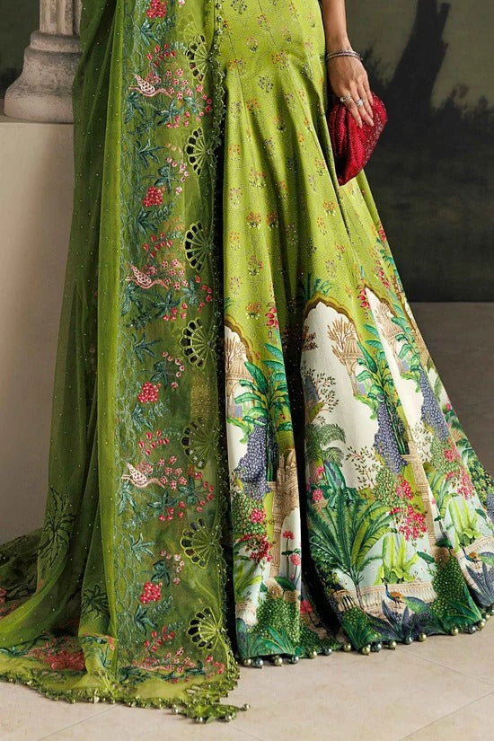 A close-up of a green traditional dress with intricate floral embroidery and a multicolor printed border, shown on a model holding a red clutch.
