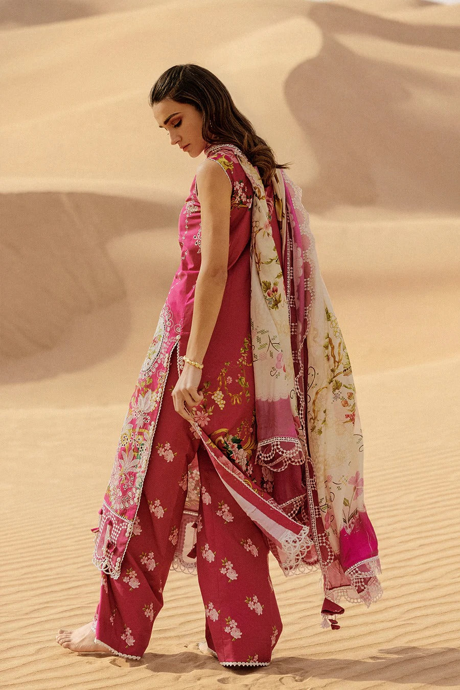 Woman in a pink traditional outfit with a floral scarf standing in sand dunes