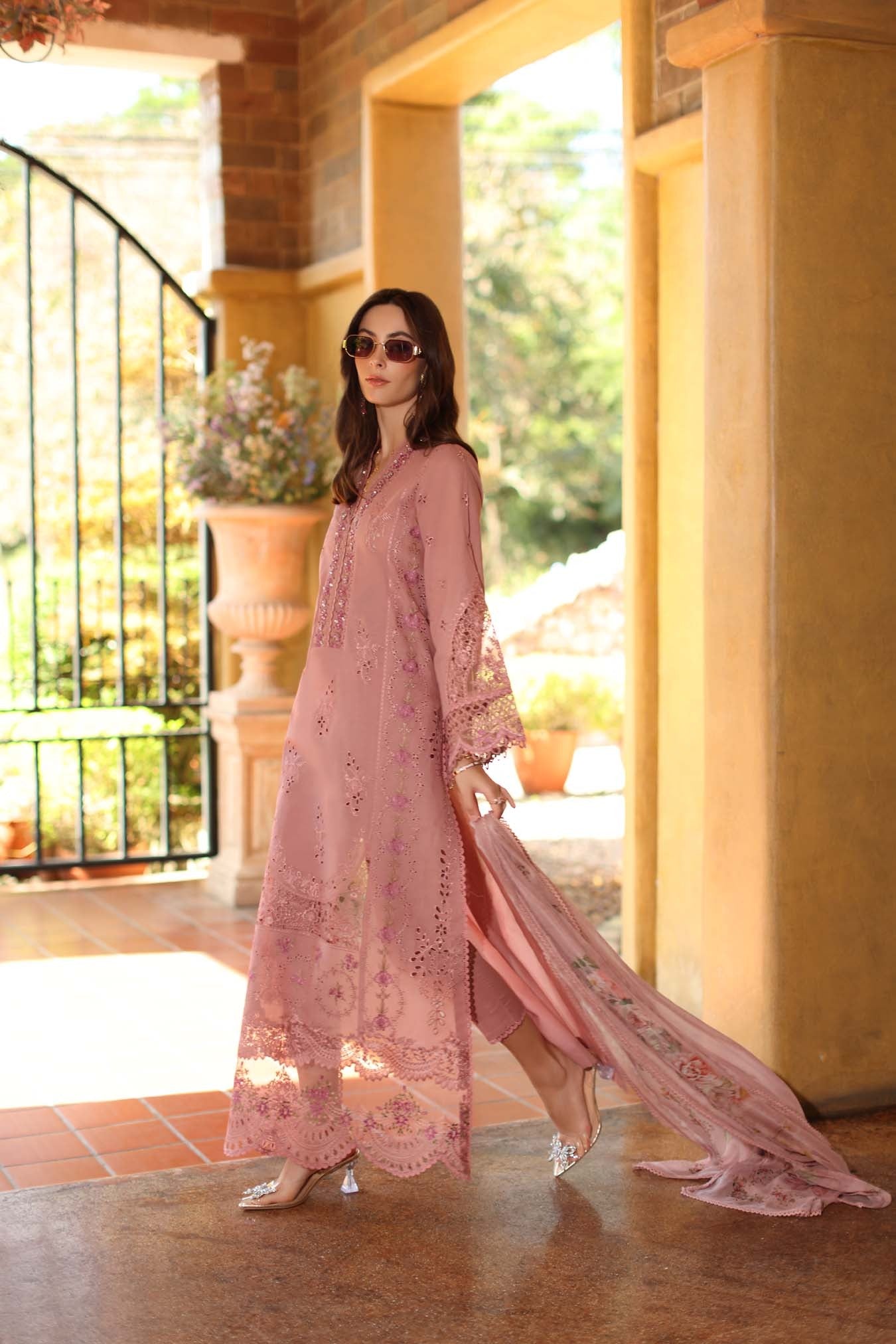 Woman in a pink lace dress standing in a sunlit room with large windows.