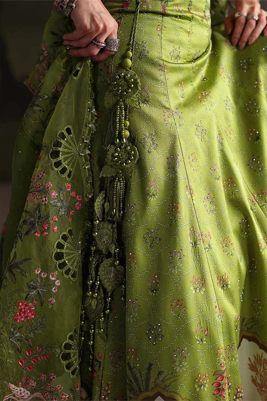 Close-up of a green embroidered traditional garment with floral patterns, mirror work, and dangling embellishments, shown on a person whose hands are visible holding the fabric.