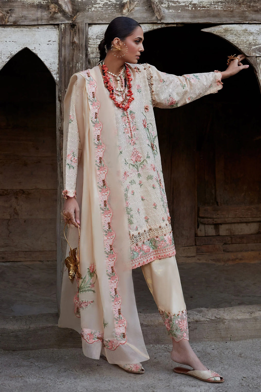 Woman in a traditional embroidered outfit standing in front of a rustic wooden archway.