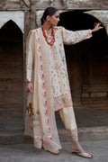 Woman in a traditional embroidered outfit standing in front of a rustic wooden archway.