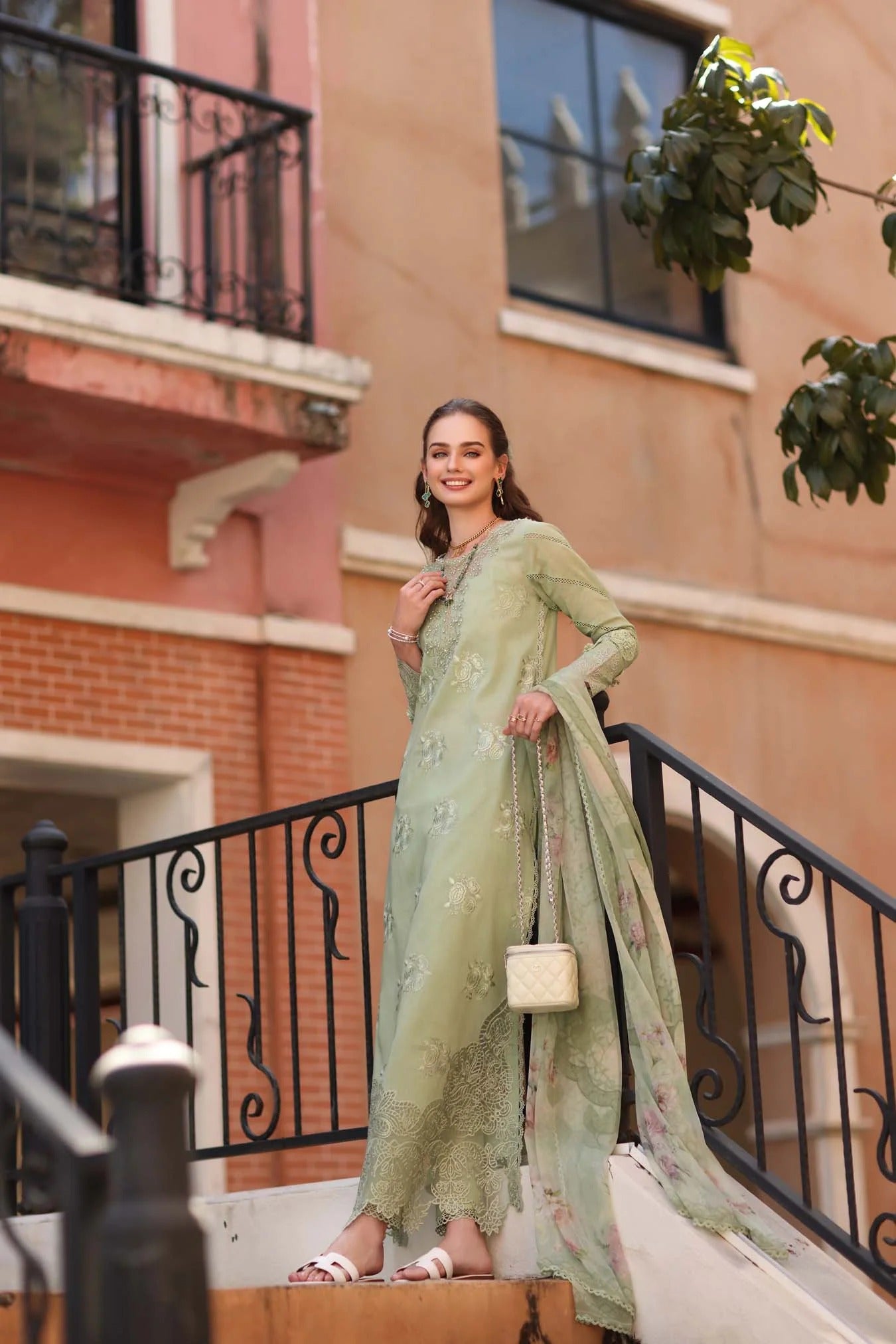 Woman in a green traditional outfit standing on a staircase with a building in the background
