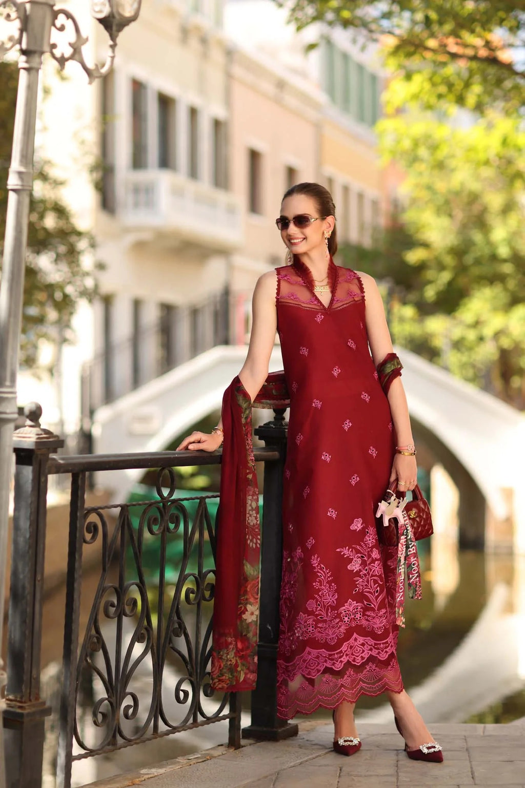 Woman in a red dress standing on a street with buildings and greenery in the background