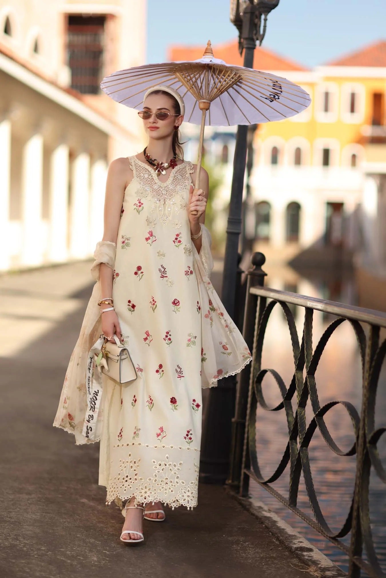 Woman in a floral dress holding an umbrella on a bridge with buildings in the background