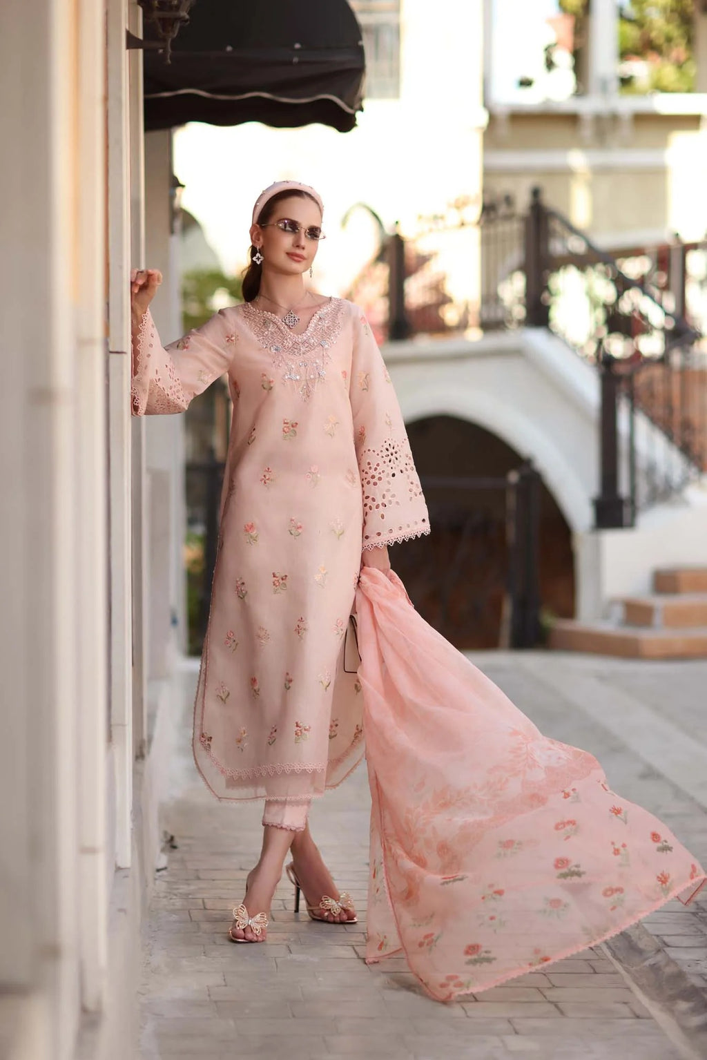Woman in a light pink traditional outfit standing outdoors.