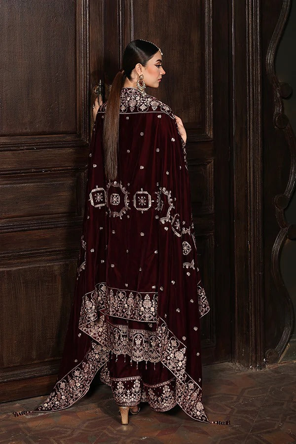 Woman in a dark red embroidered traditional outfit standing against a wooden door.