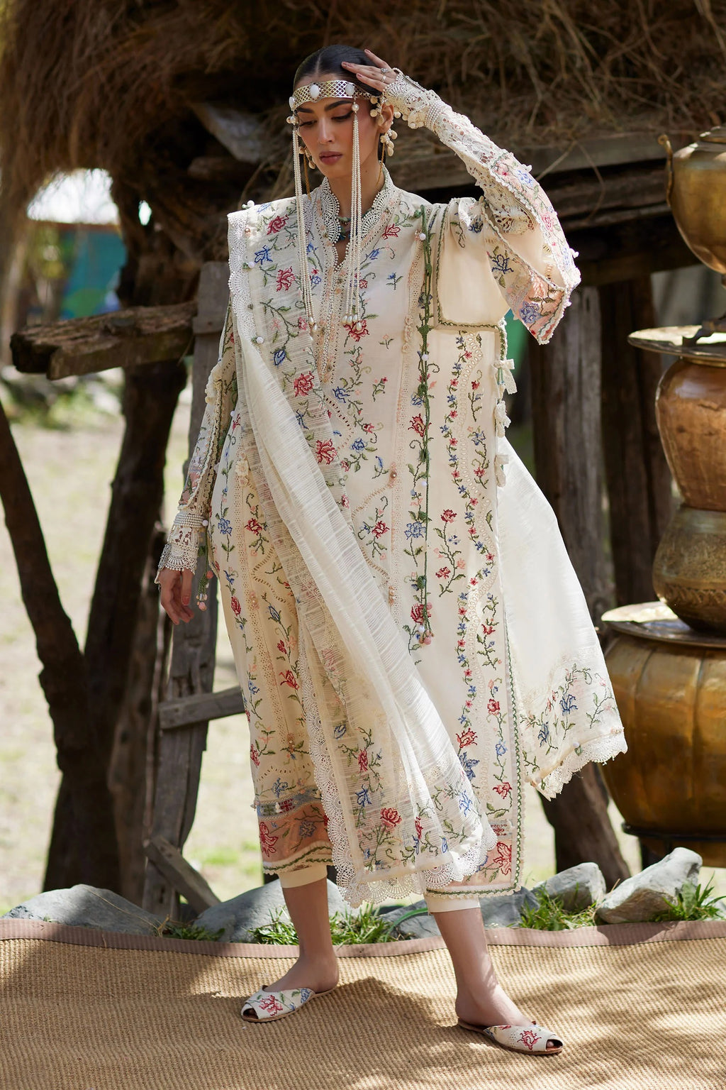 Woman in a traditional embroidered outfit standing outdoors with a rustic background.