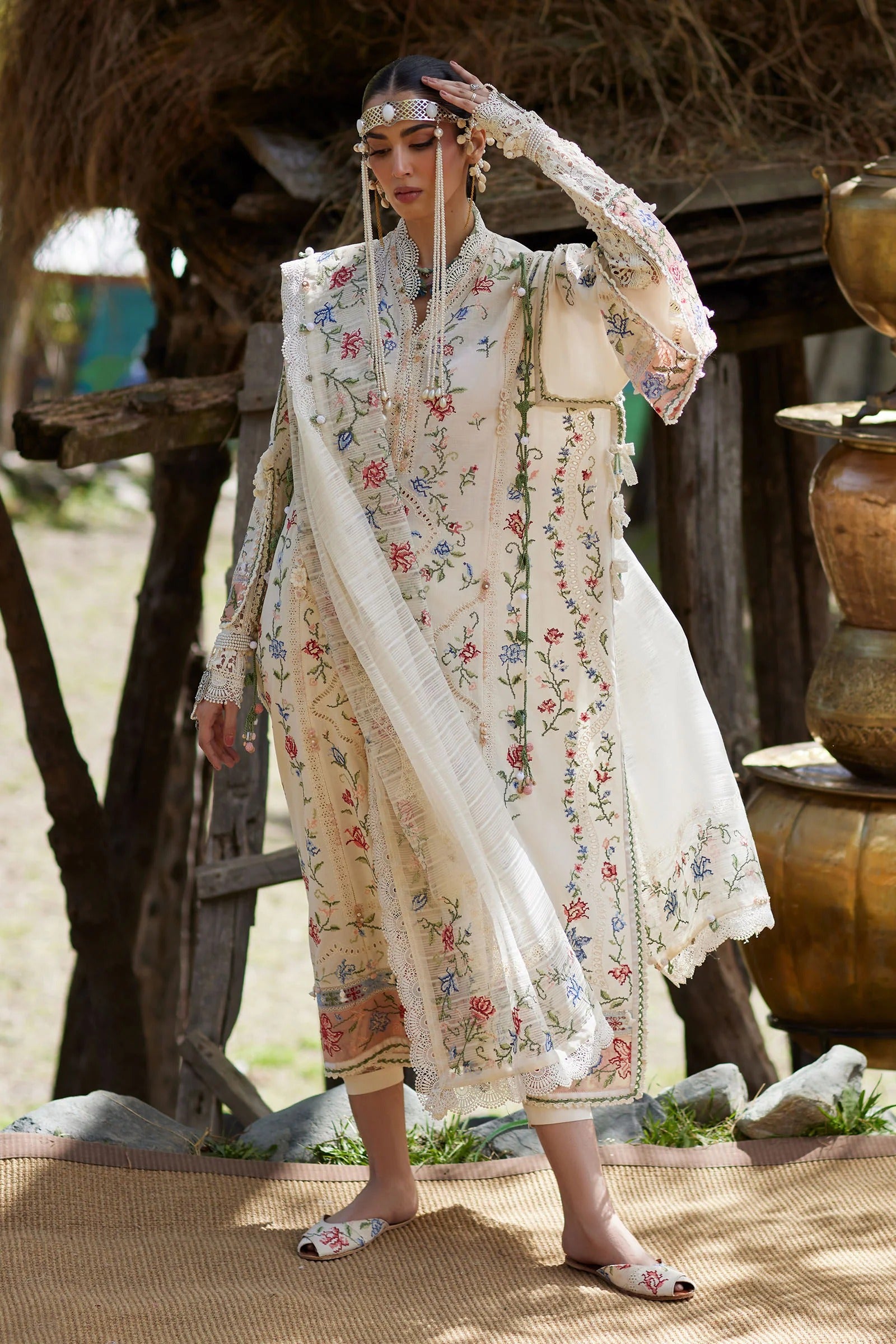 Woman in a traditional embroidered outfit standing outdoors with a rustic background.