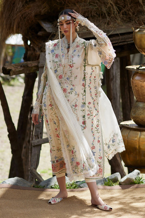 Woman in a traditional embroidered outfit standing outdoors with a rustic background.