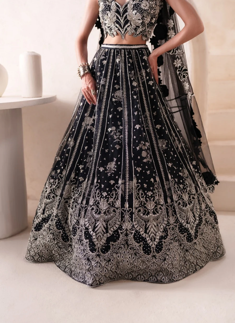 A black and silver embellished lehenga choli set with a matching dupatta, shown on a model in an indoor setting.