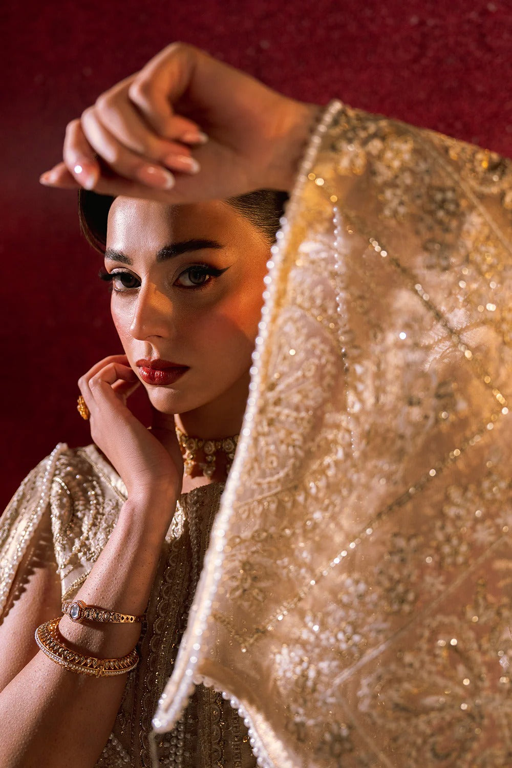 Woman wearing a gold dress with intricate patterns, posing against a red background.
