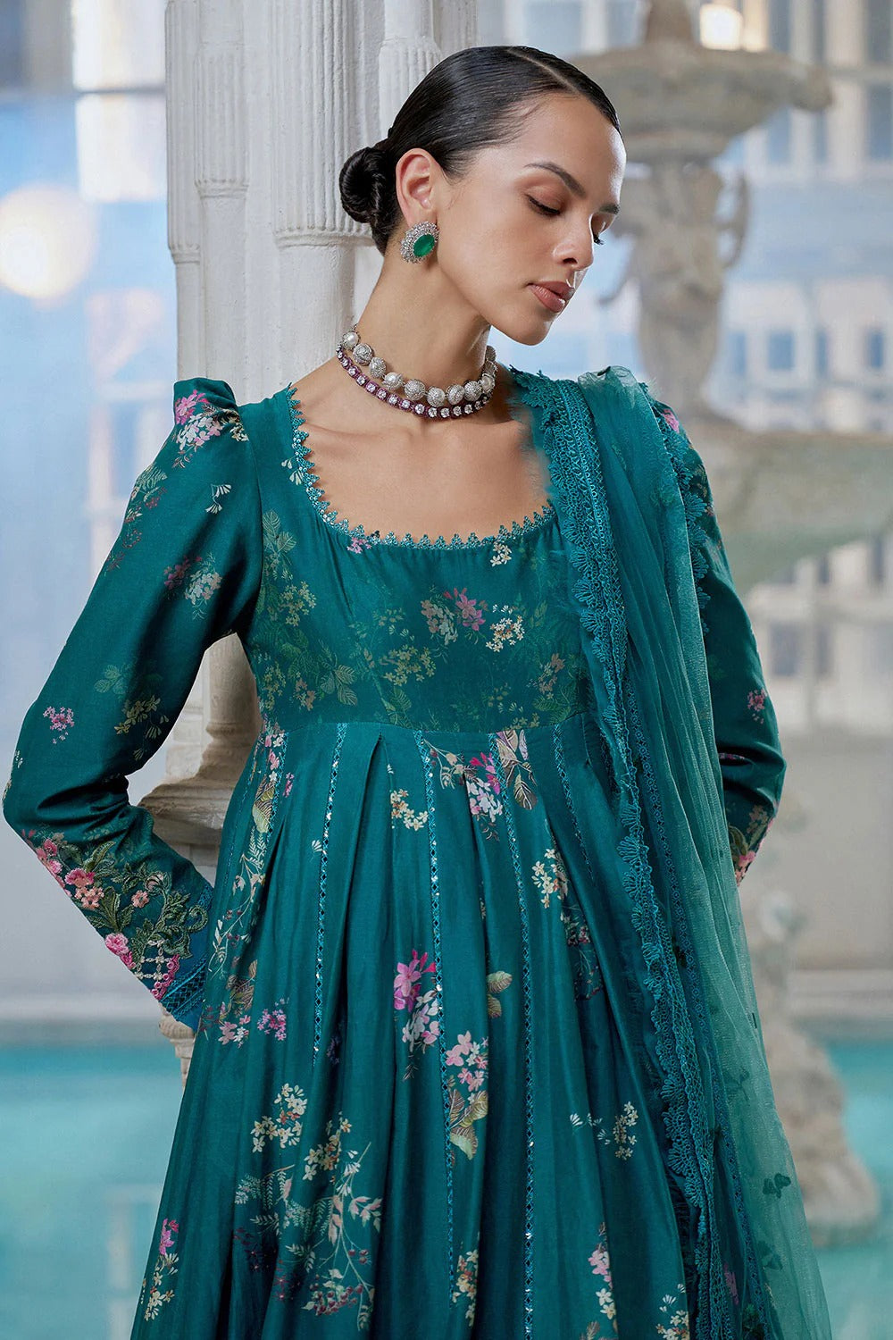 Woman wearing a teal floral dress with a matching shawl in an elegant indoor setting.