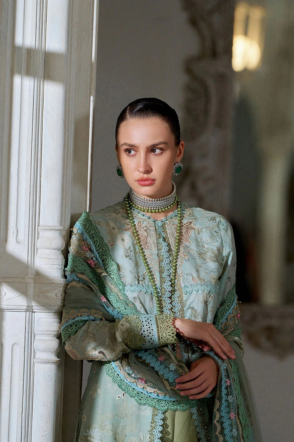 Woman in an ornate dress with intricate patterns and jewelry, standing indoors.