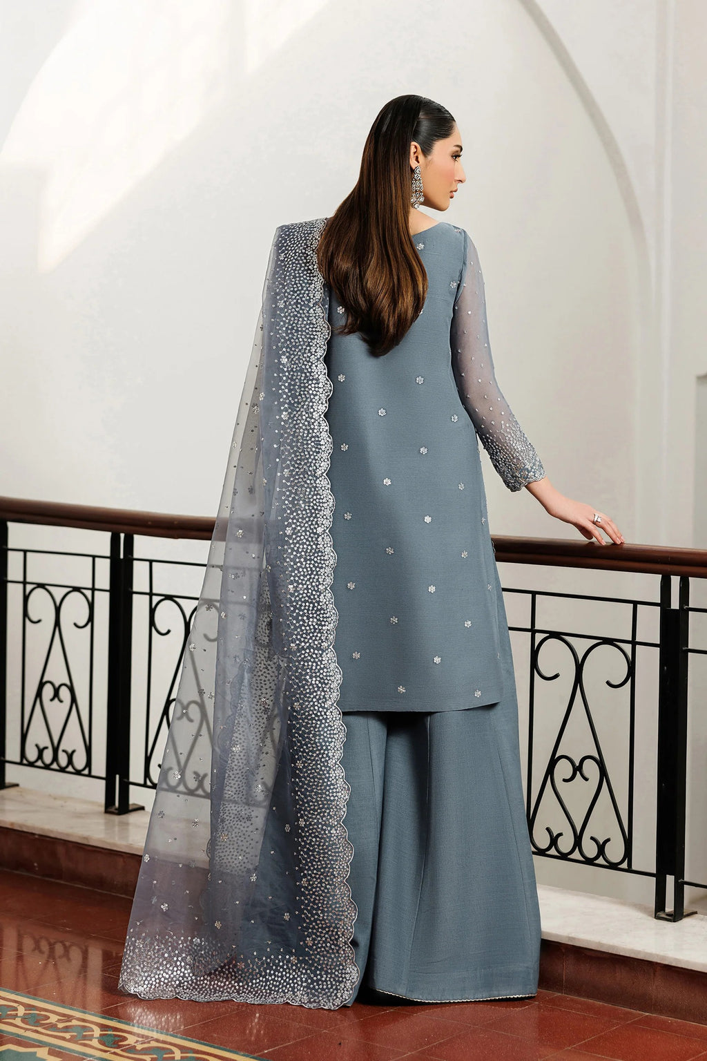 Woman in a gray traditional outfit with a long scarf in an elegant interior setting